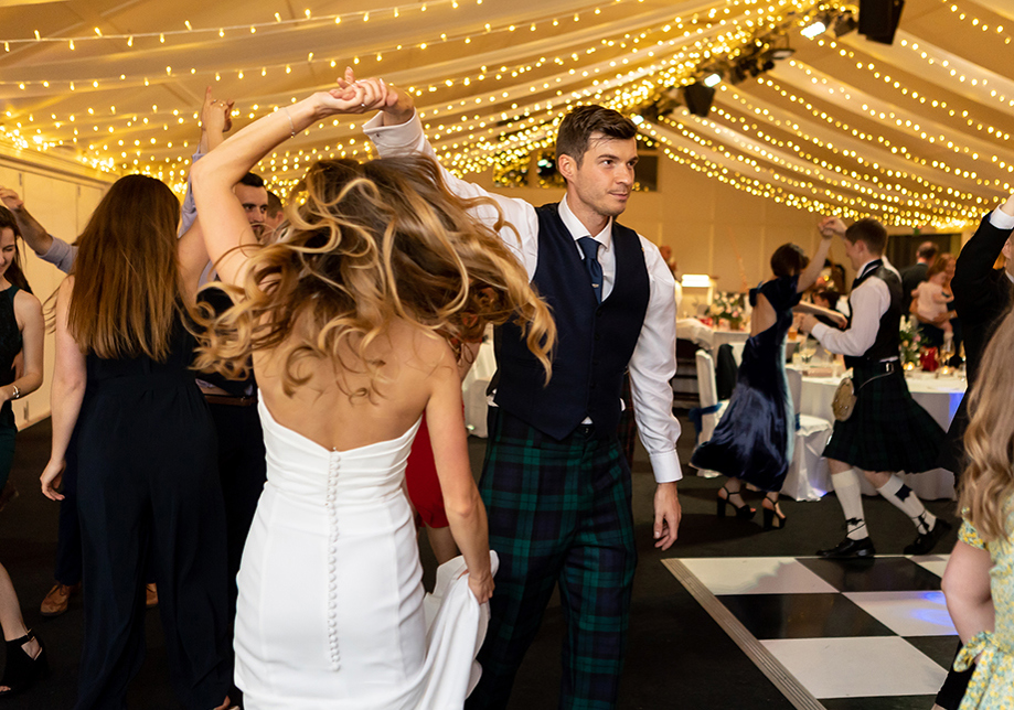 Bride and groom dancing under draped fairy light ceiling